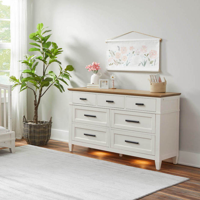 A white dresser with drawers beside a Heritage House Artisan 4-in-1 Convertible Crib in a nursery setting.