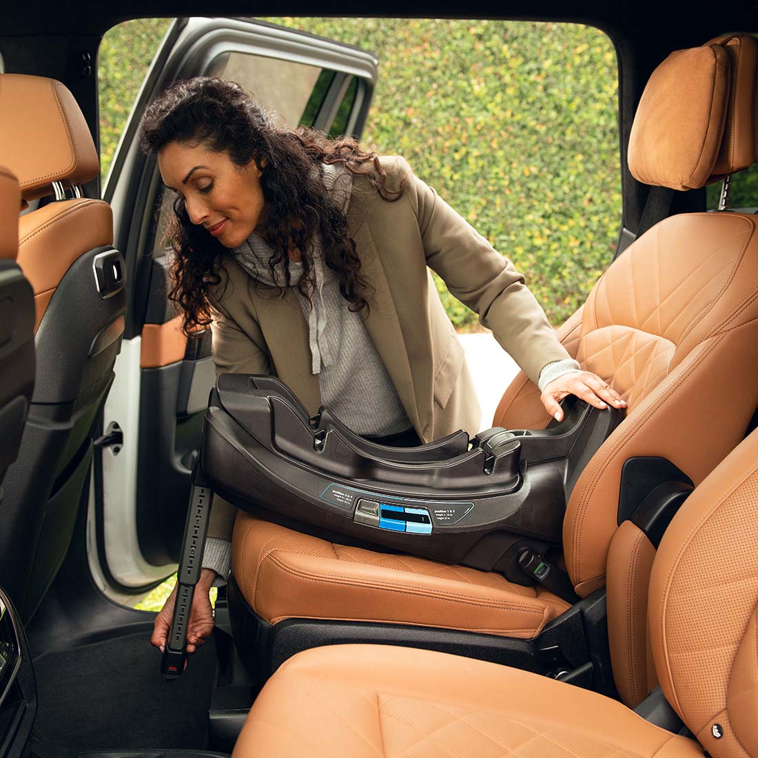 Woman adjusting pipa car seat base in a vehicle with brown leather interior.